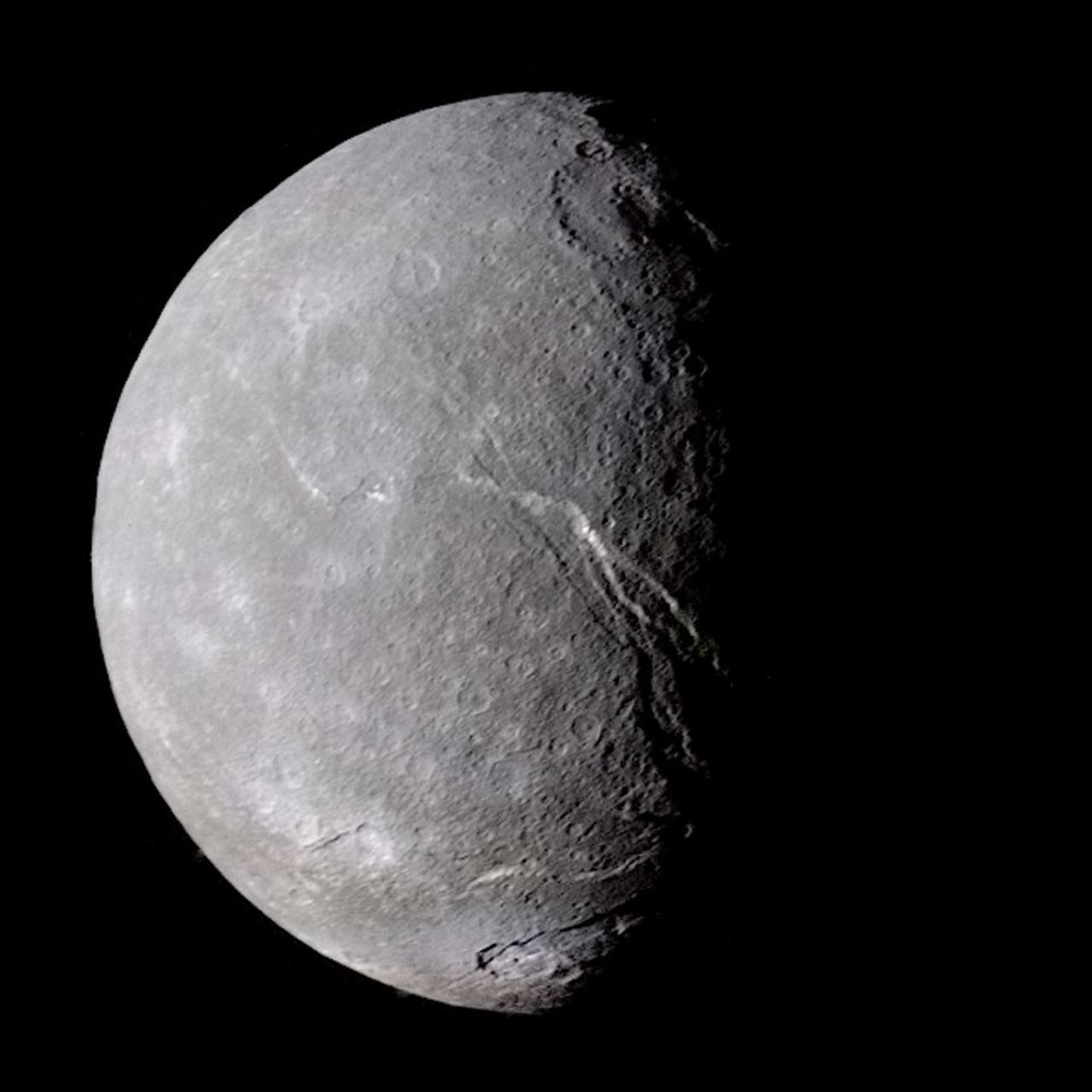 A half-lit moon is shown that is unfamiliar. The moon appears mostly gray but with some light patches. Two large craters appear near the terminator, and some large cracks are also evident. Please see the explanation for more detailed inform