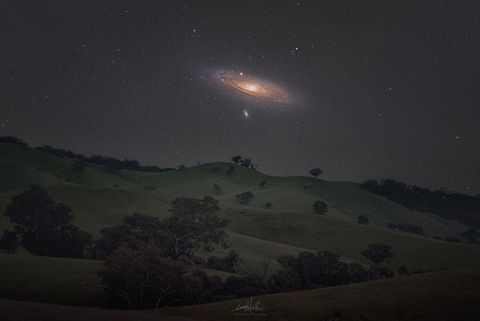 The Andromeda galaxy above rolling hills.