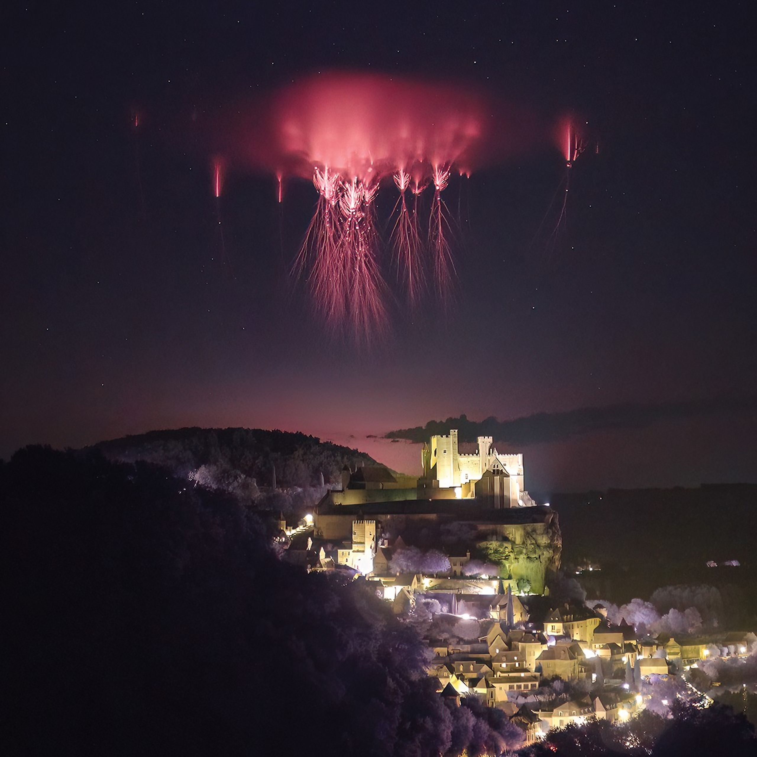 Fotografía nocturna que muestra un "sprite" o duende rojo, un fenómeno eléctrico atmosférico superior poco común, que aparece como un destello carmesí sobre el castillo de Beynac, en Dordoña, Francia. El duende se extiende verticalmente en el cielo oscuro sobre las nubes de tormenta, capturado por Nicolas Escurat, participante del proyecto de ciencia ciudadana Spritacular de la NASA.