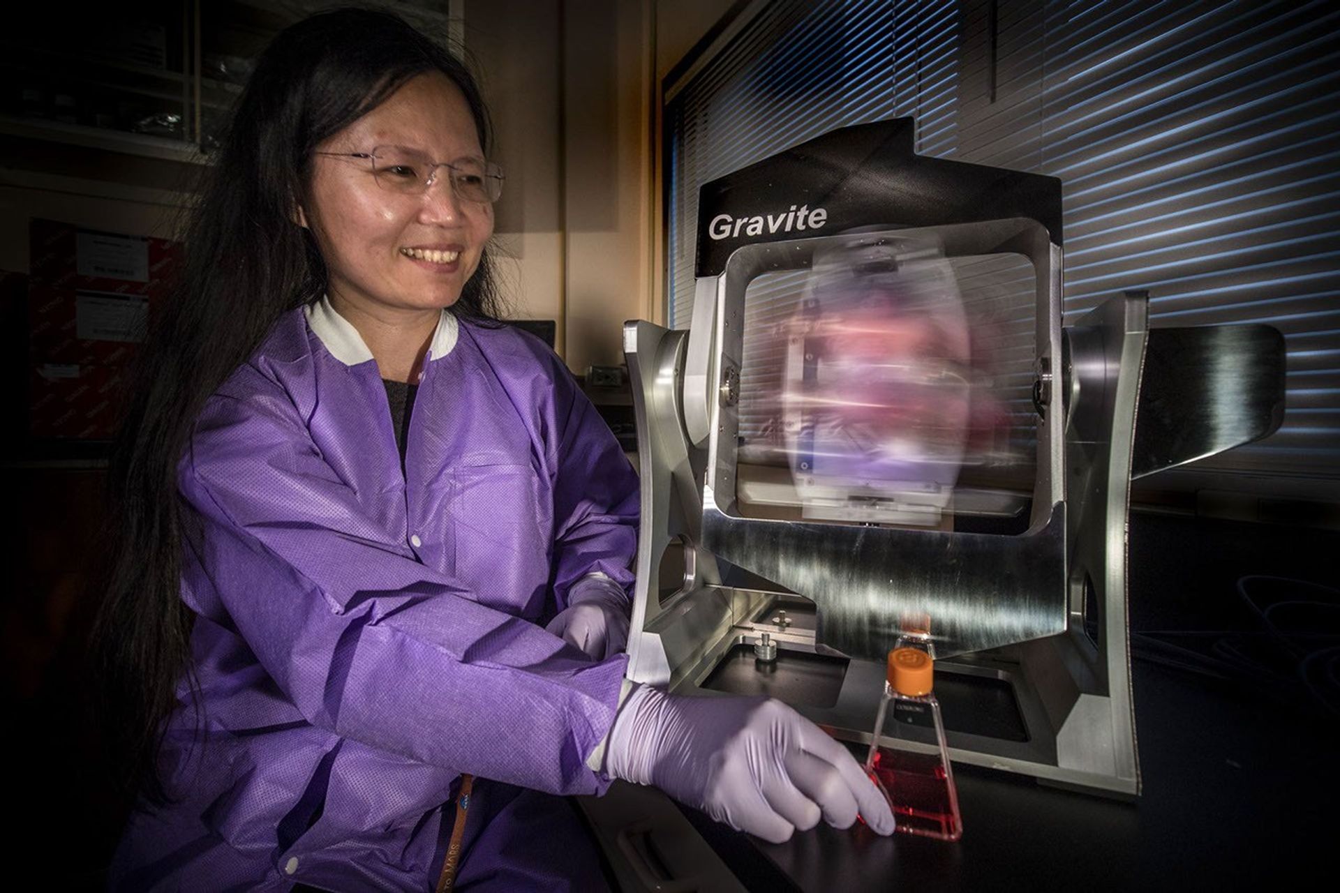 La doctora Ye Zhang, científica del proyecto para la Oficina de Investigación de la EEI en el Centro Espacial Kennedy de la NASA en Florida, demuestra cómo se llevan a cabo las pruebas con muestras biológicas en un dispositivo de simulación de microgravedad.