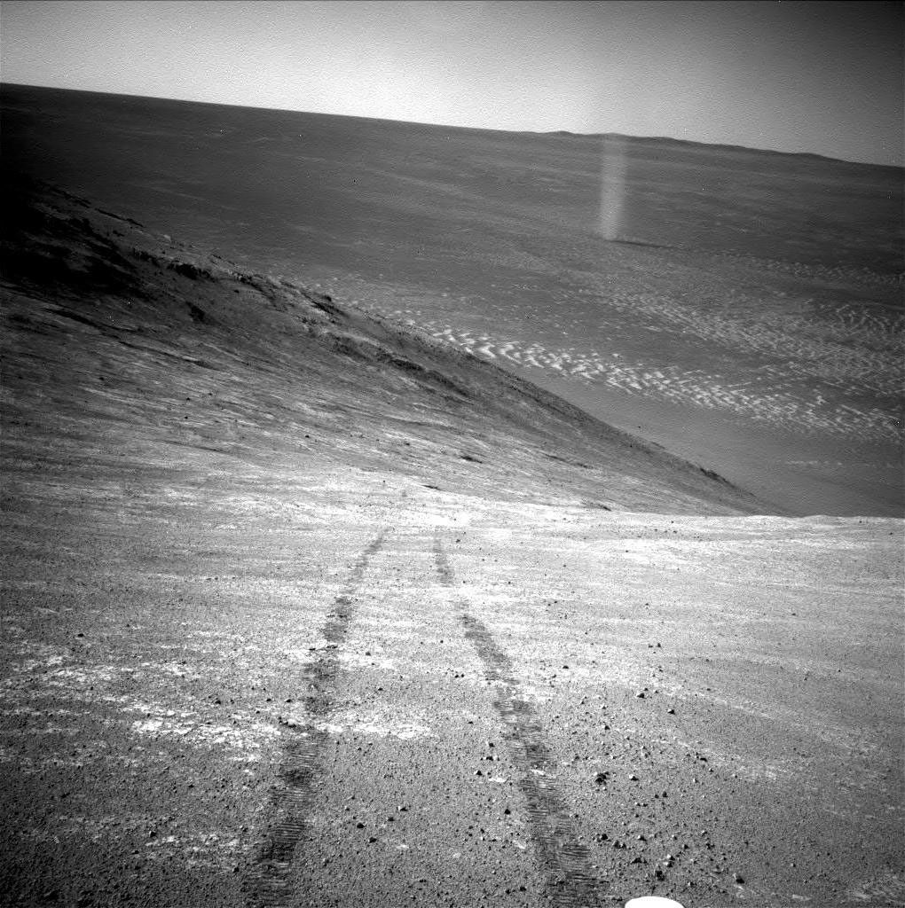 Imagen en blanco y negro del terreno marciano, con huellas de un rover en el medio, captada desde la superficie por el rover de la NASA Opportunity.