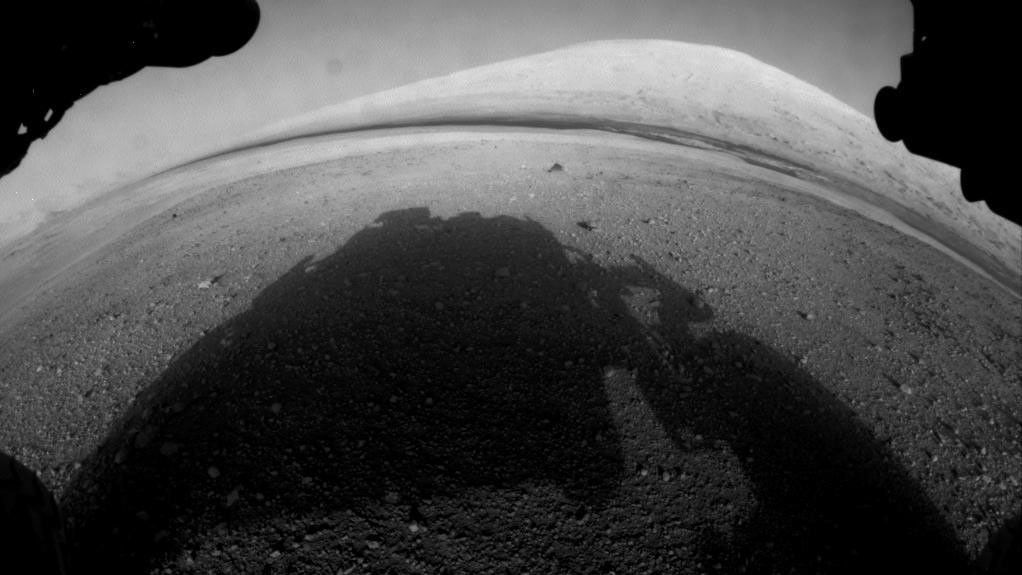 Imagen en blanco y negro del suelo marciano captada por el rover de la NASA Curiosity, con su propia sombra proyectada en medio de la imagen.