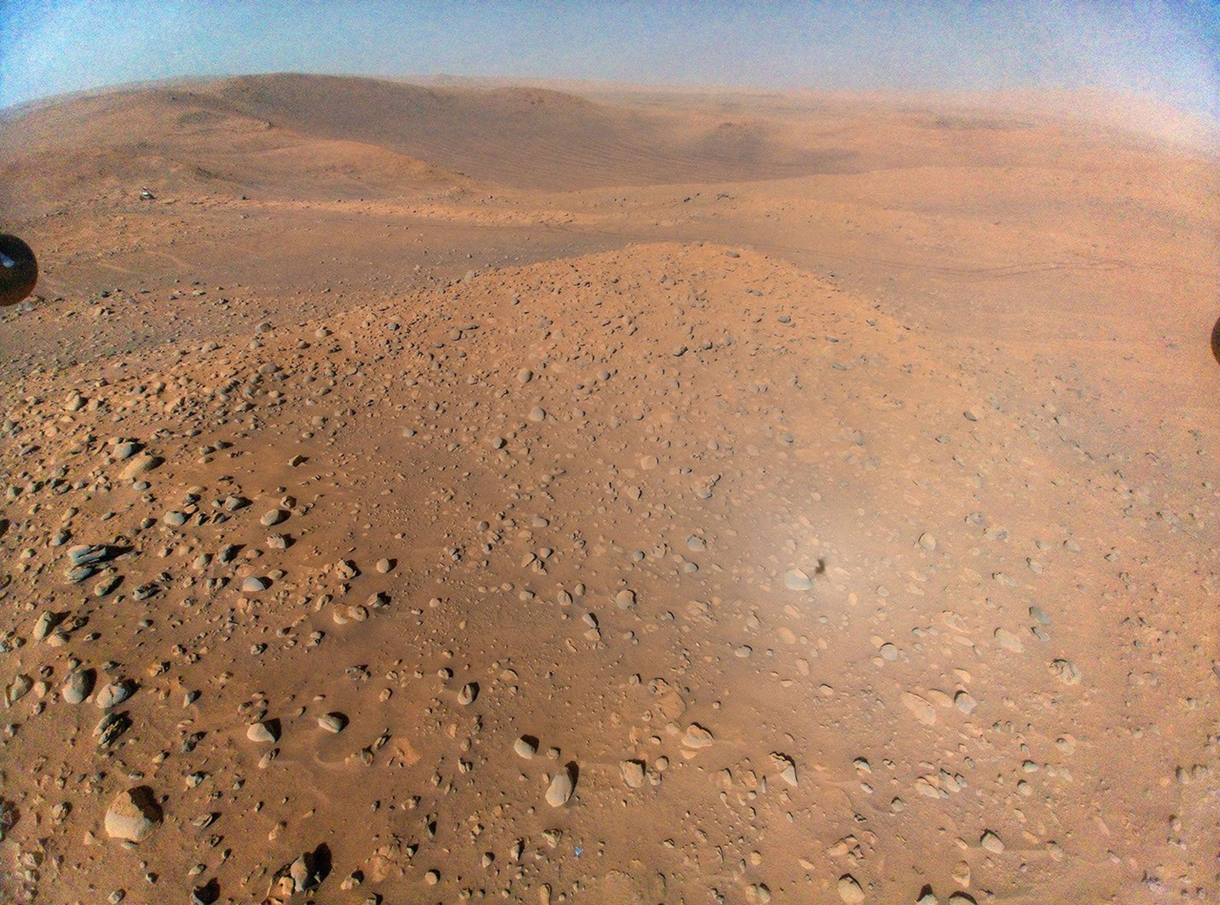 Esta vista desde Ingenuity, tomada desde una altitud de unos 12 metros (40 pies) durante su vuelo número 51, incluye al rover, visible como una mancha blanquecina en la parte superior izquierda.