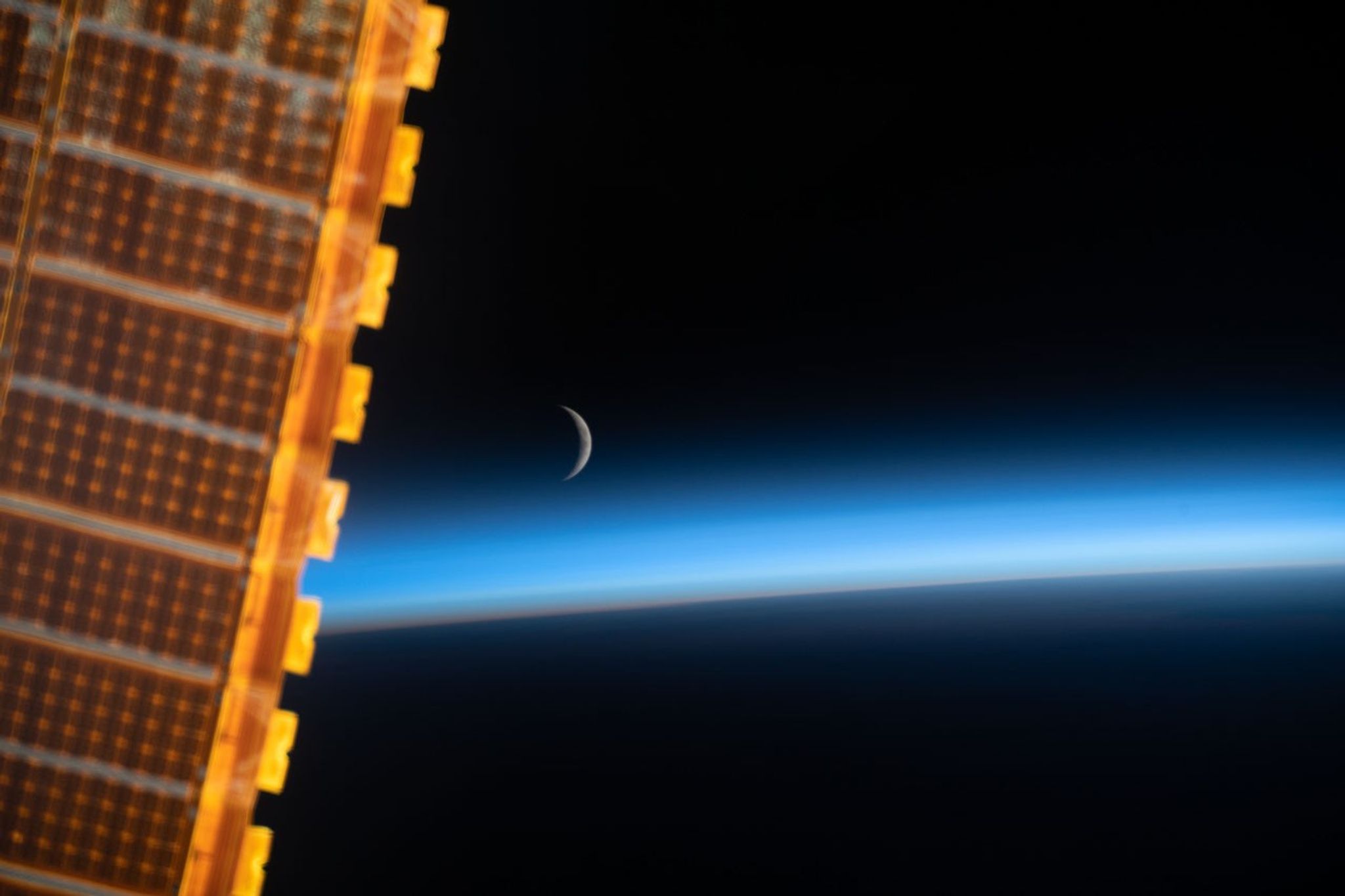 La luna creciente aparece justo por encima de la atmósfera de la Tierra mientras la Estación Espacial Internacional orbita el planeta.