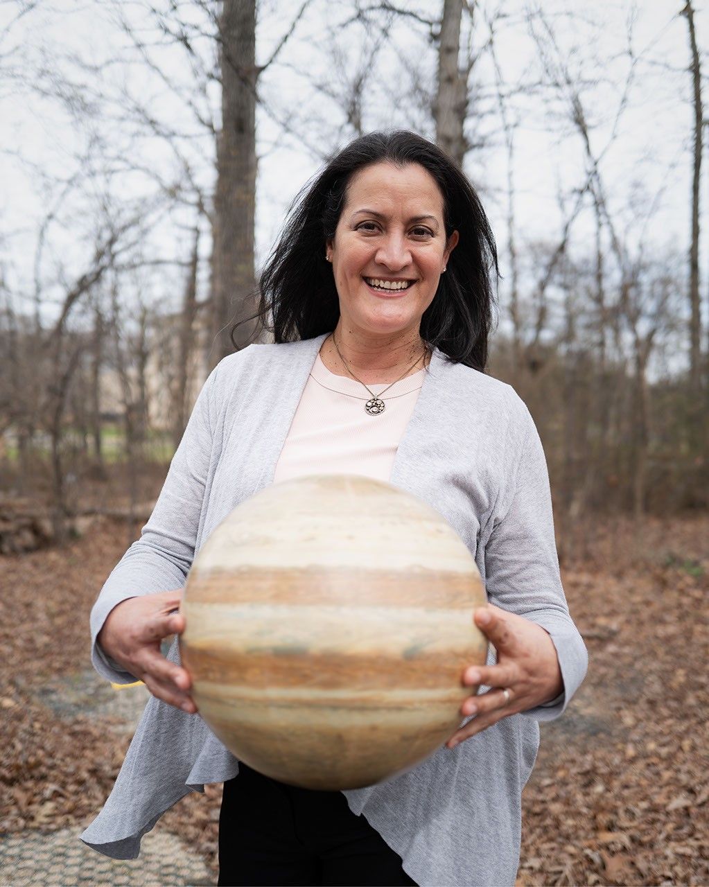 Dr. Delia Santiago-Materese outside of her office, holding a model of Jupiter.