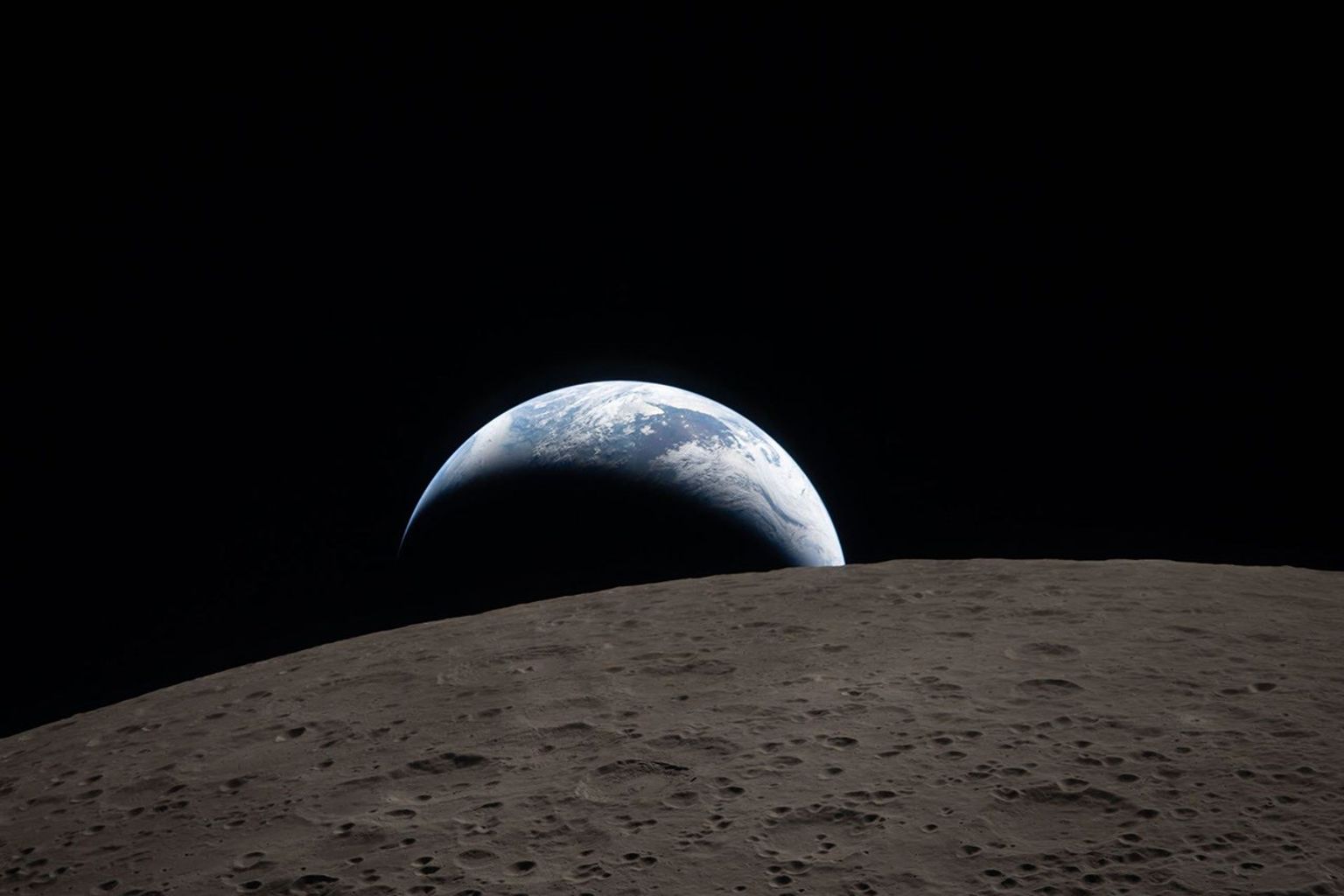 La Tierra parece esconderse tras el horizonte lunar. El fondo es negro.