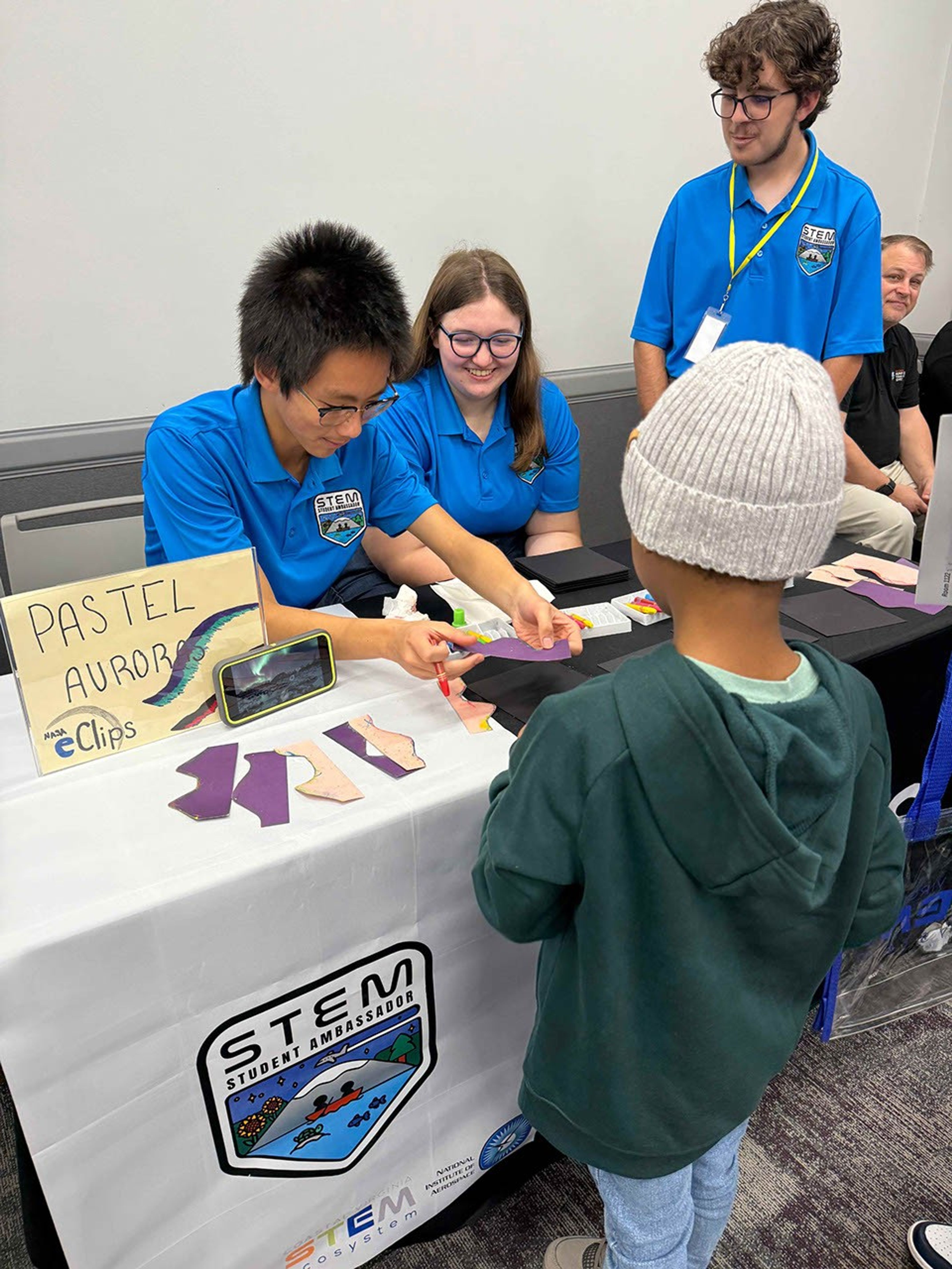 STEM Ambassadors assist a young boy in making a pastel aurora.