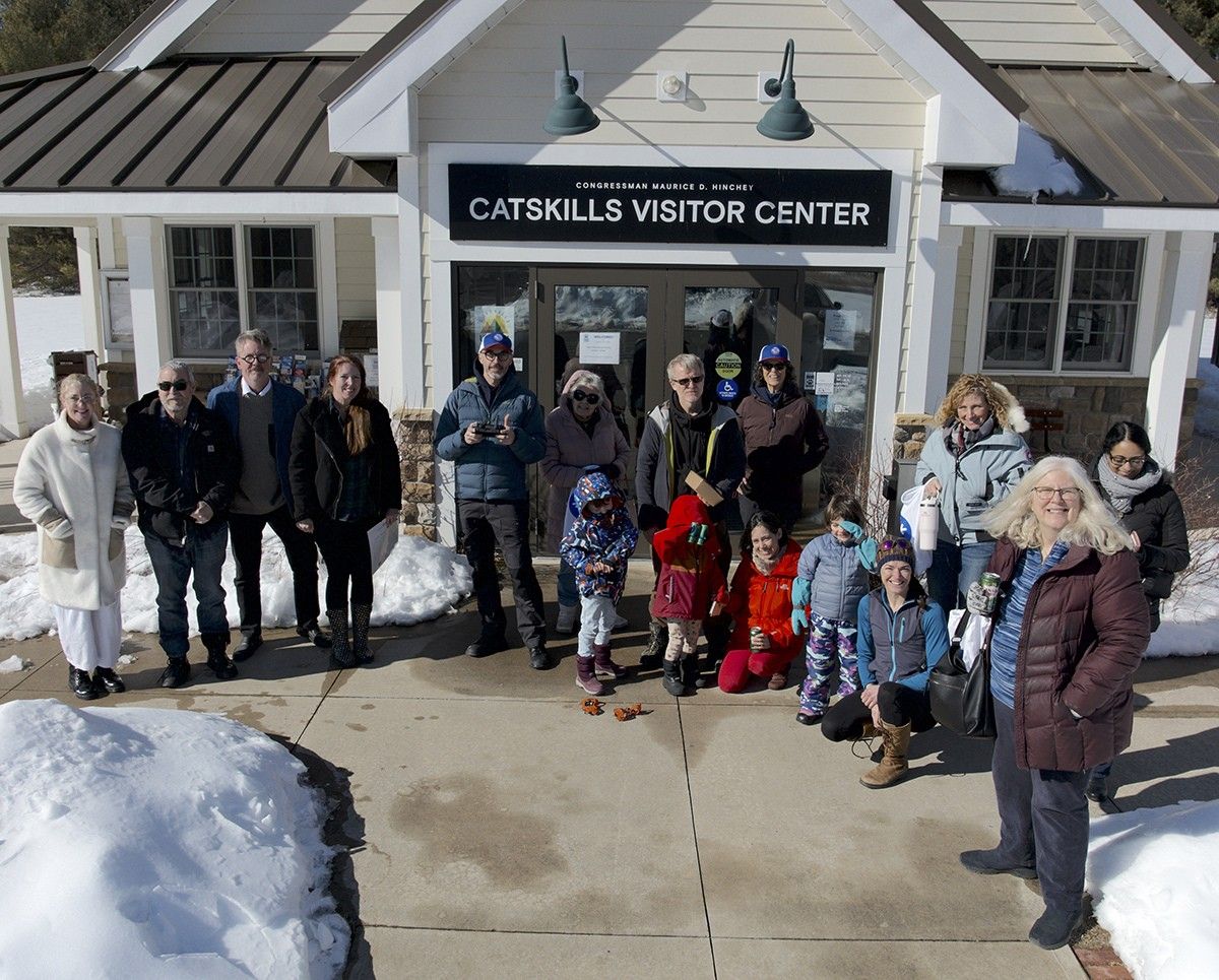 Group of people, including adults and children, gathered outside the Catskills Visitor Center on a snowy day, dressed in winter clothing.