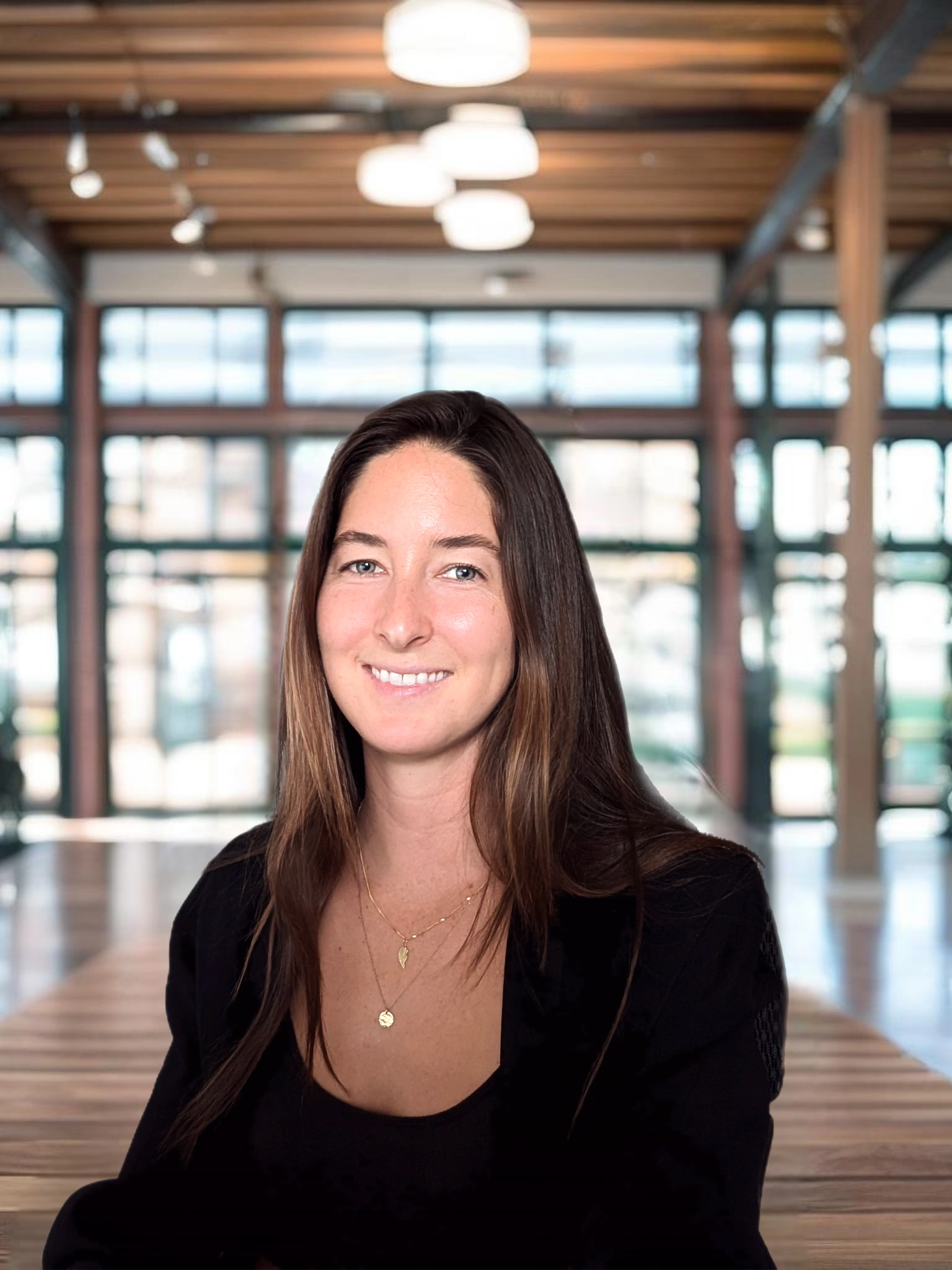 Headshot of Ariel Deutsch indoors in a spacious building with large windows and soft overhead lighting, wearing a dark jacket.