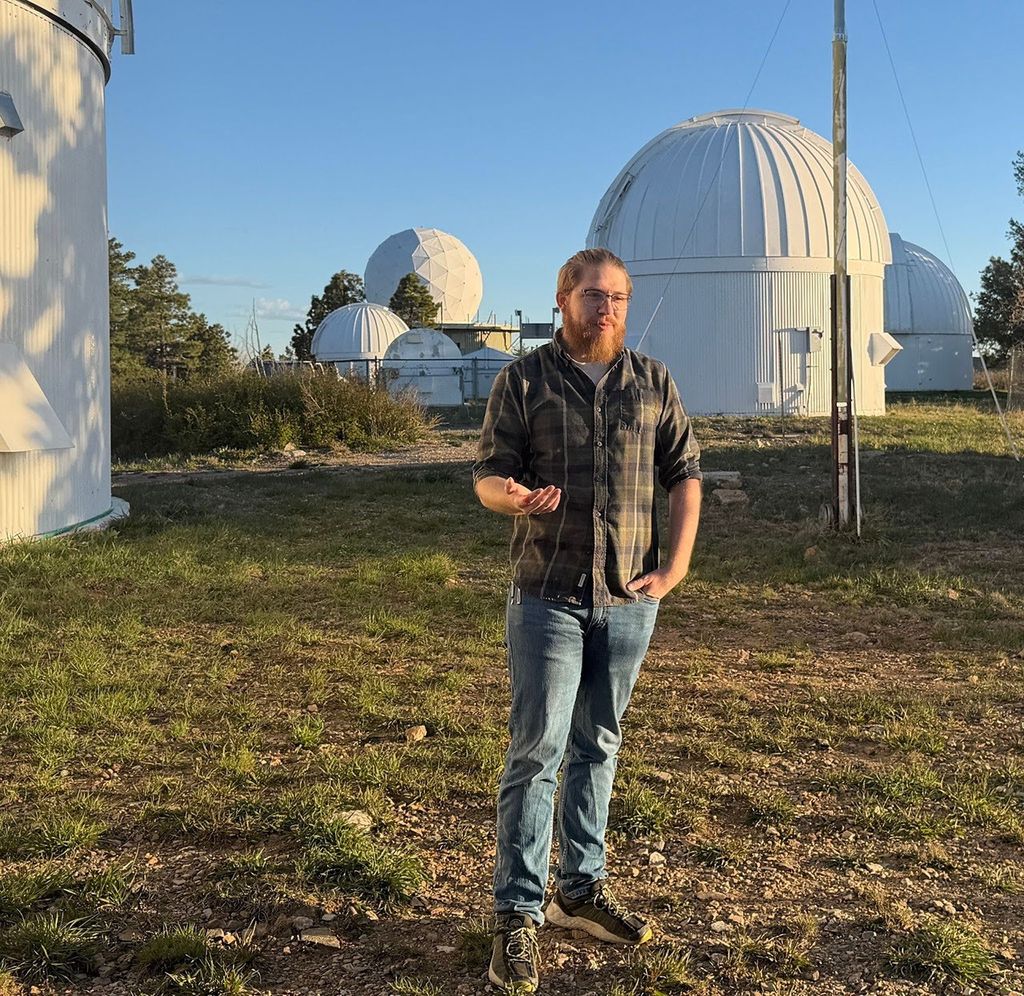 A person standing outside next to a white telescope dome with three more visible in the background.
