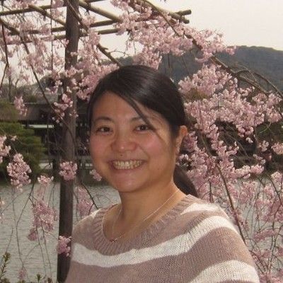 Portrait photo of a smiling woman standing in front of a blossoming cherry tree