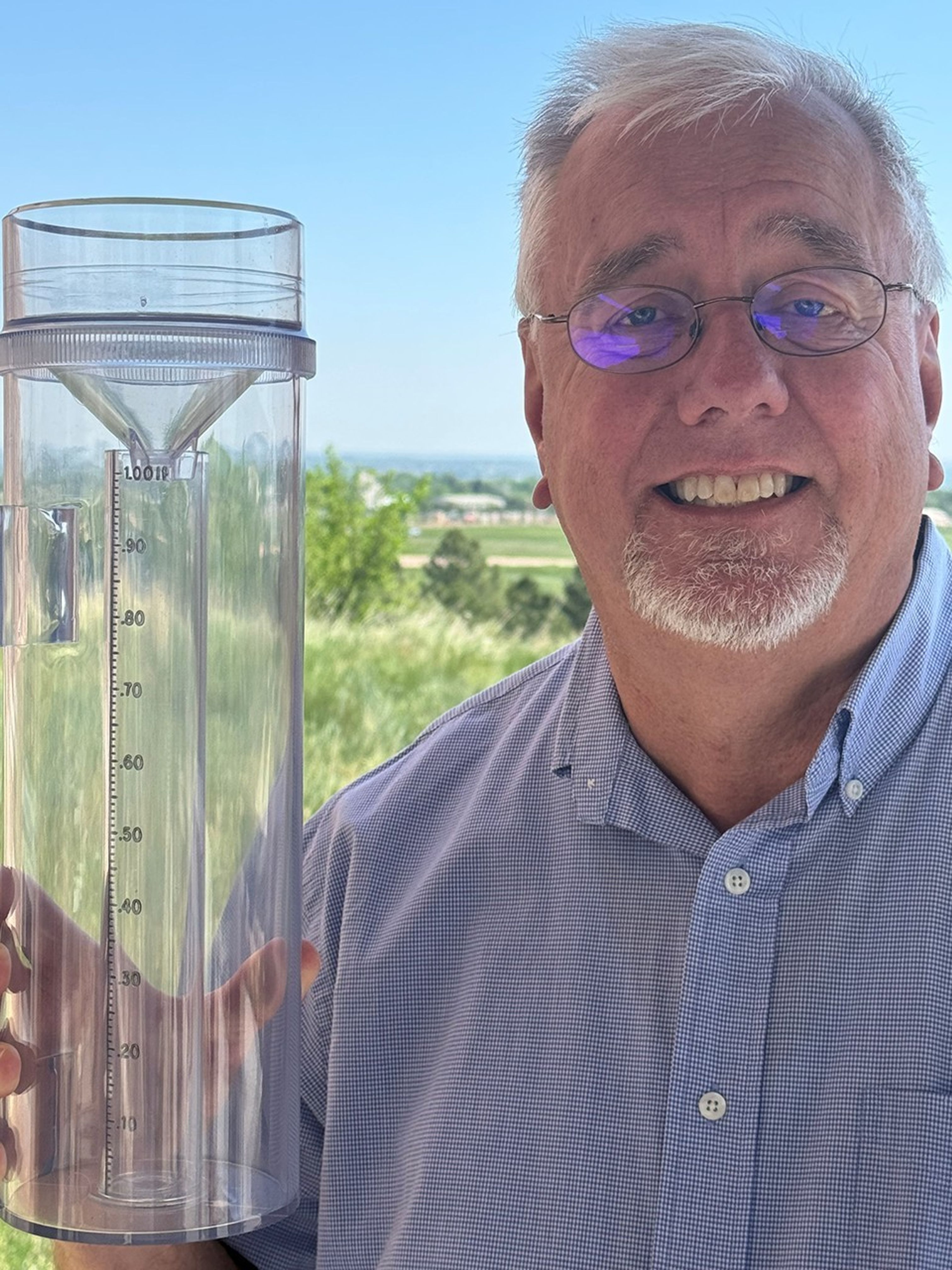 White man in blue shirt holds up a rain and snow gauge.