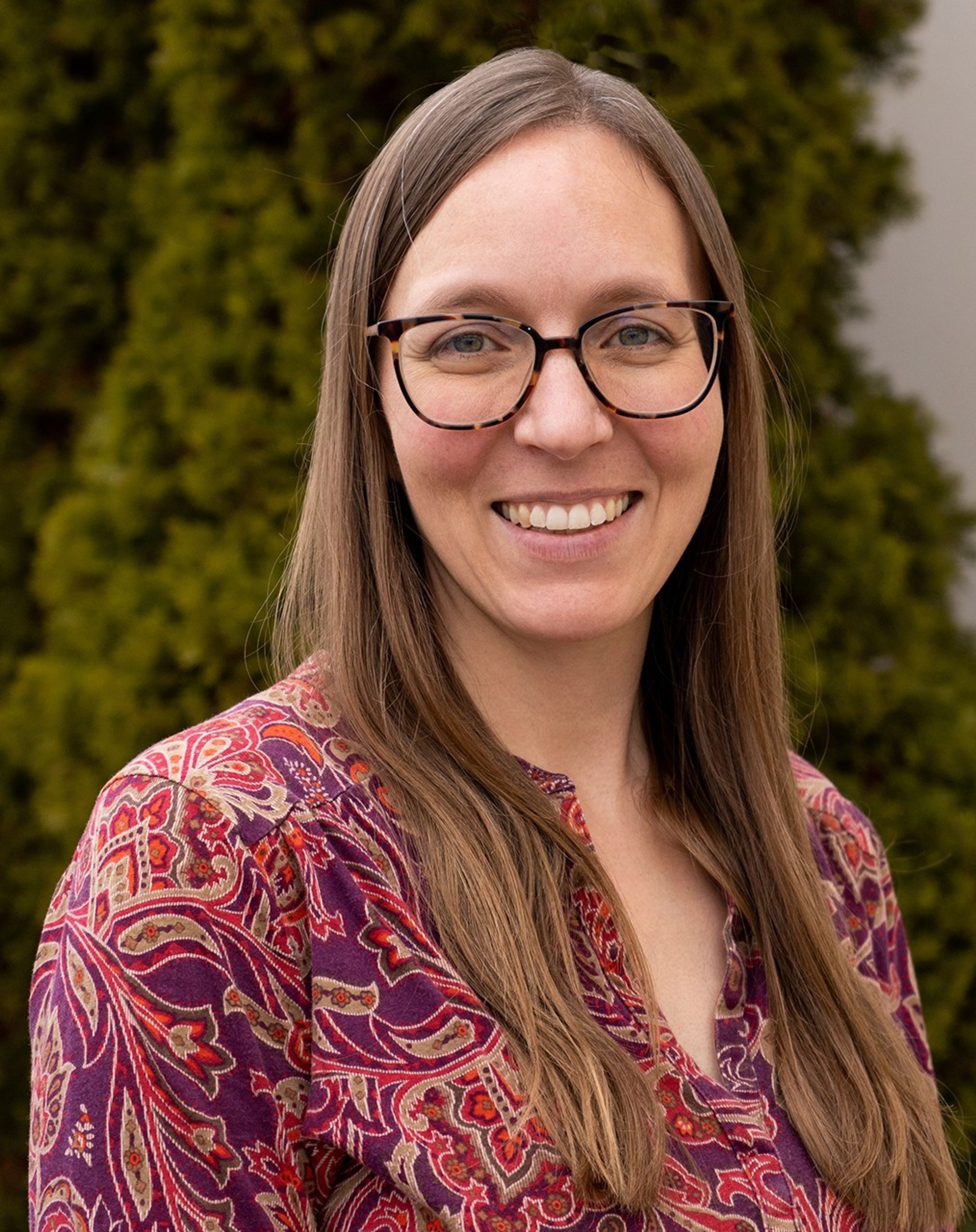 Portrait photo of a smiling woman wearing glasses with green trees in the background