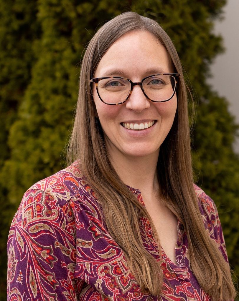Portrait photo of a smiling woman wearing glasses with green trees in the background