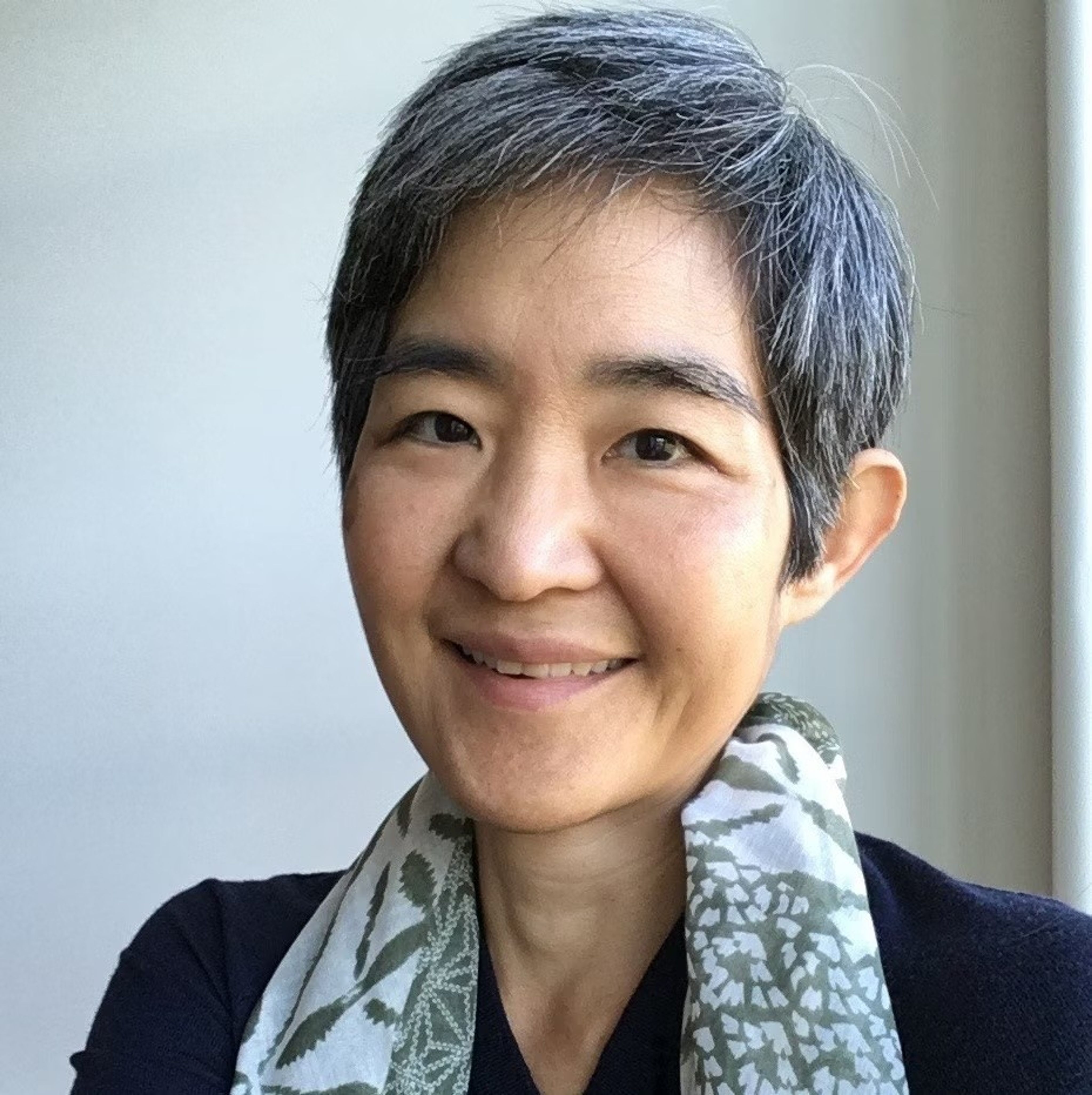 Portrait photo of a smiling woman with a short pixie cut and a scarf draped around her neck