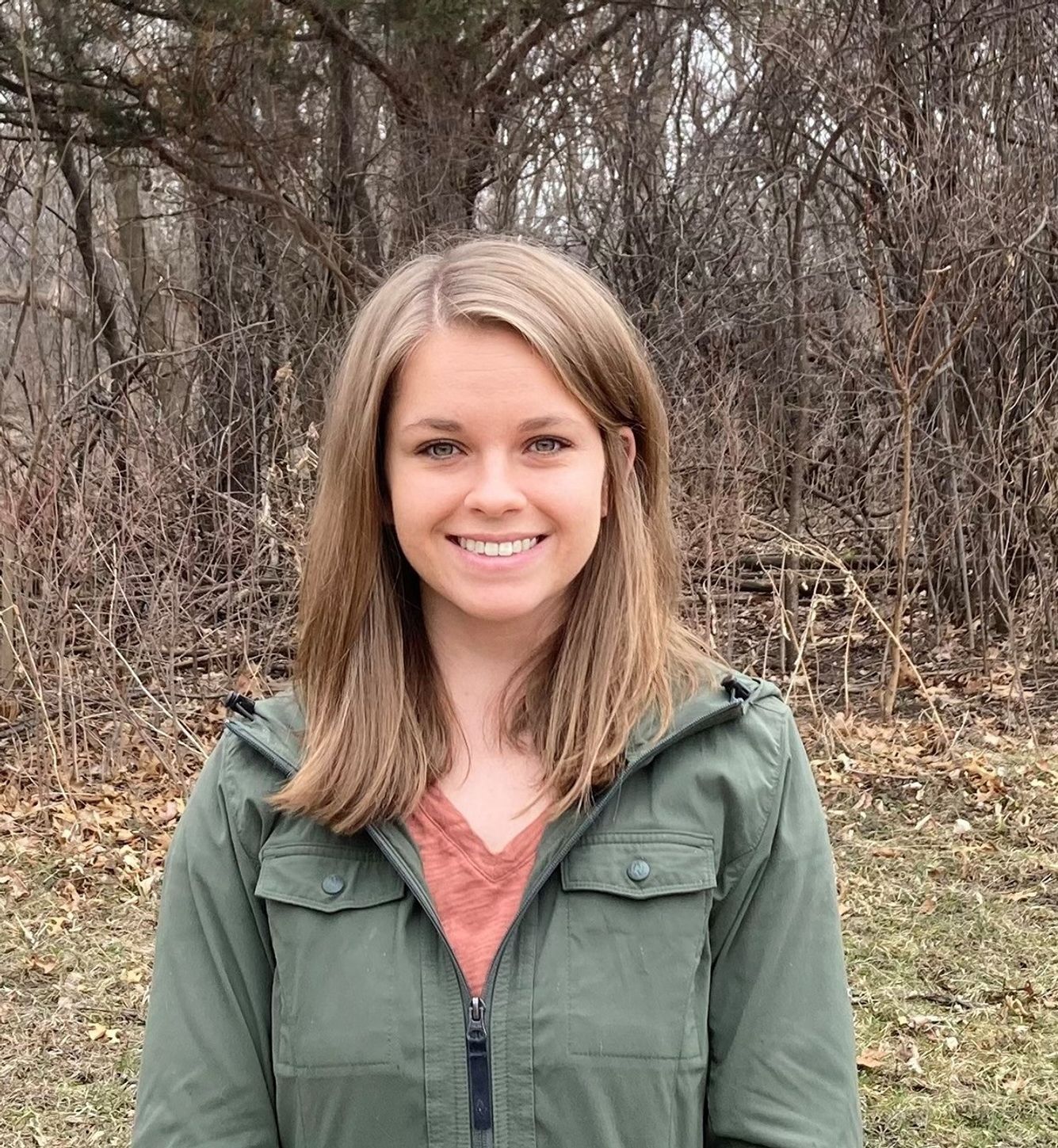 Photo of a young smiling woman standing outside with bare trees behind her