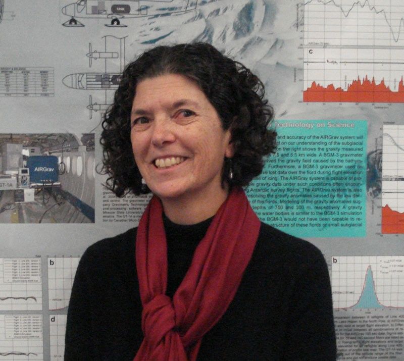Portrait photo of a smiling woman standing in front of a wall displaying data charts