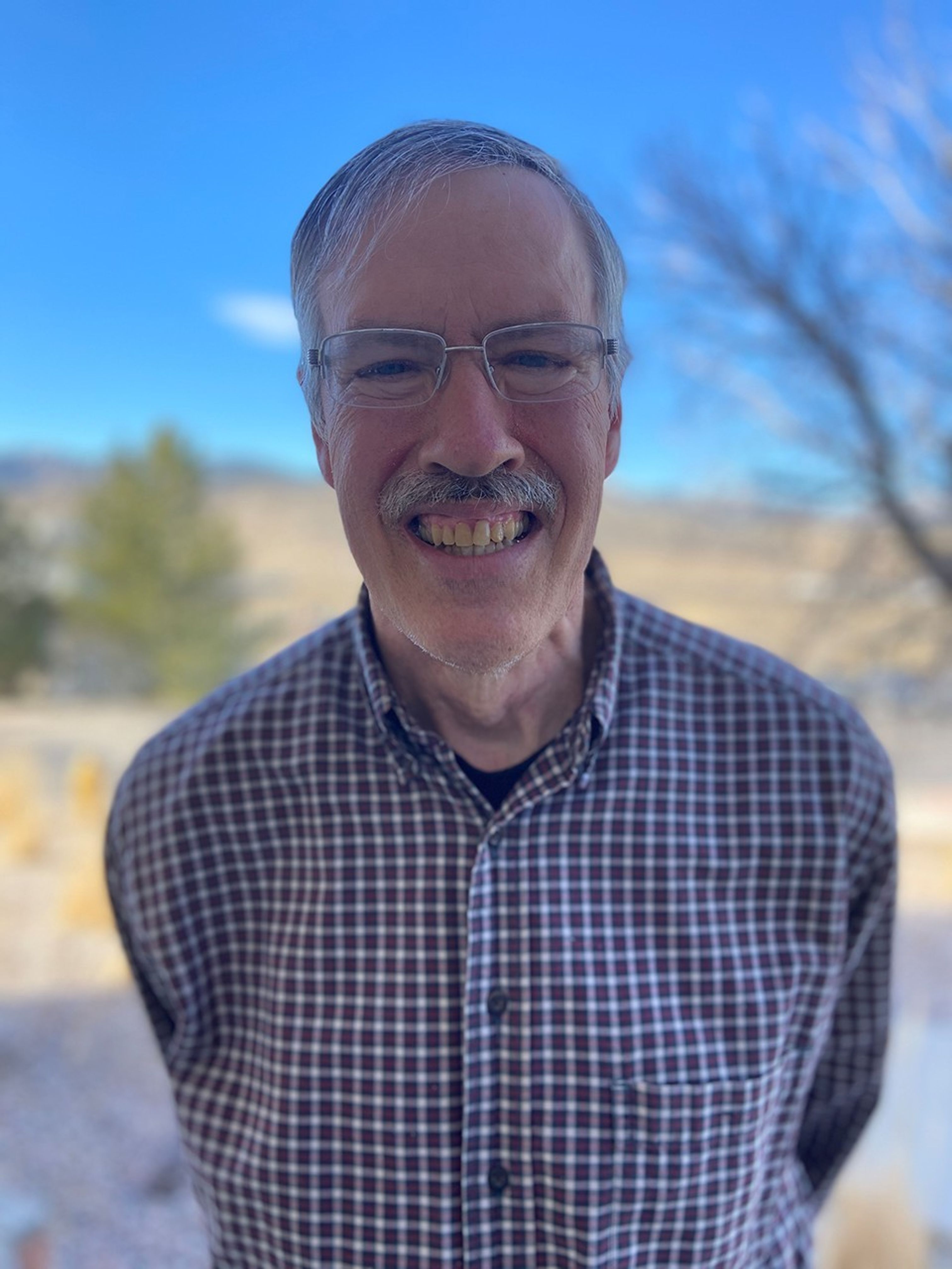 White man smiling in front of a blue sky and prairie.