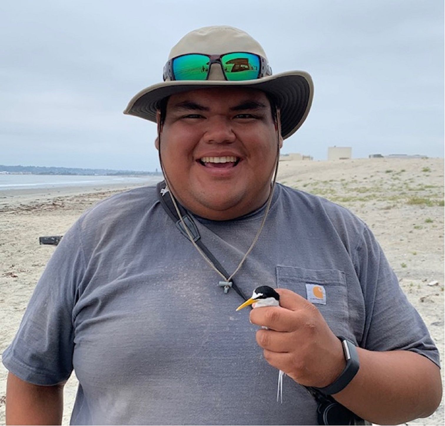Photo of a smiling man wearing a brimmed hat and holding a small bird