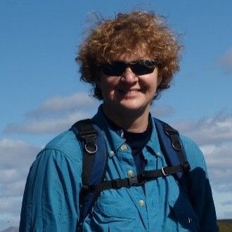 Portrait photo of a smiling person wearing sunglasses and backpack with clouds in a blue sky in the background