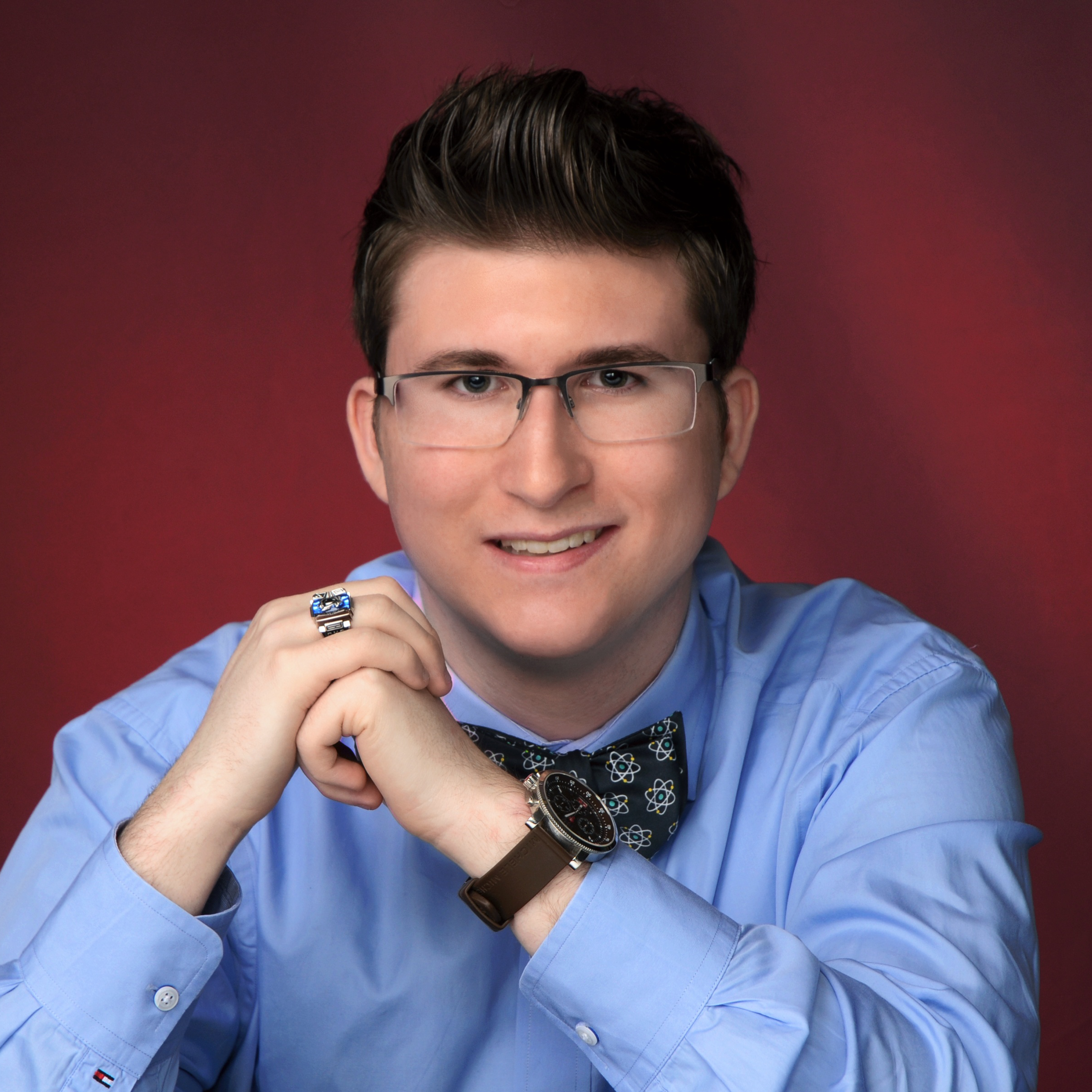 Portrait photo of a young smiling man wearing glasses and clasping his hands