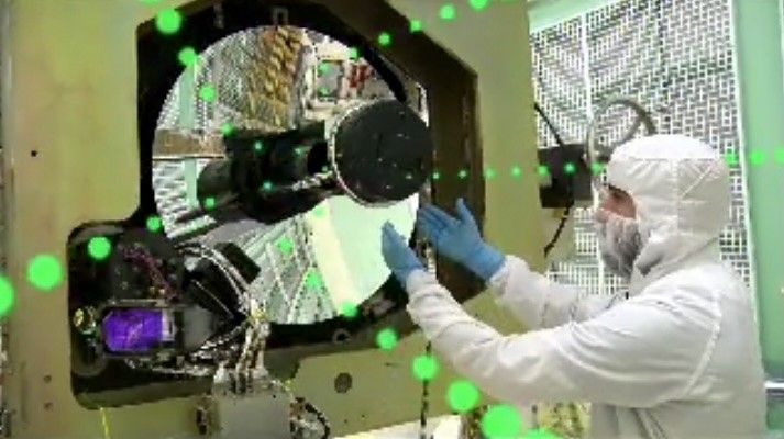 Engineer in a cleanroom suit working on a large spacecraft mirror with green laser light simulation overlaid.