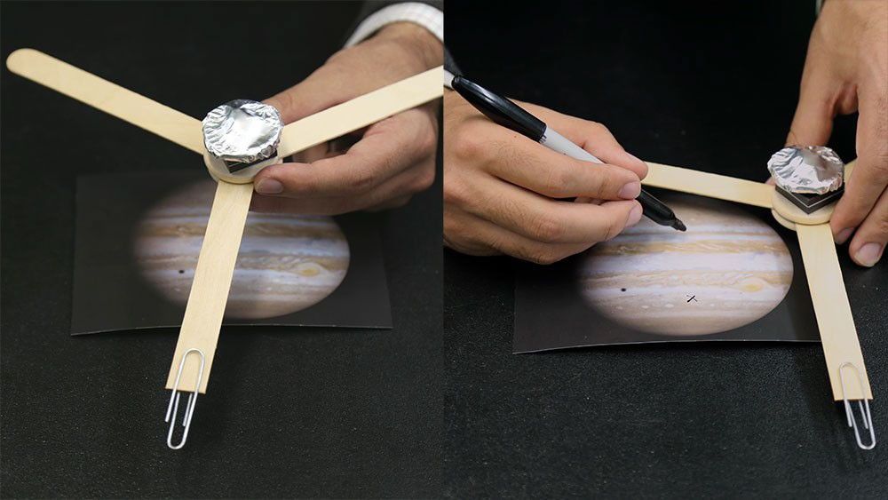 Two-step photo showing a simple homemade spacecraft model made from craft sticks, foil, and a paperclip placed on an image of Jupiter. In the second step, a person uses a marker to draw on the Jupiter image near the model.