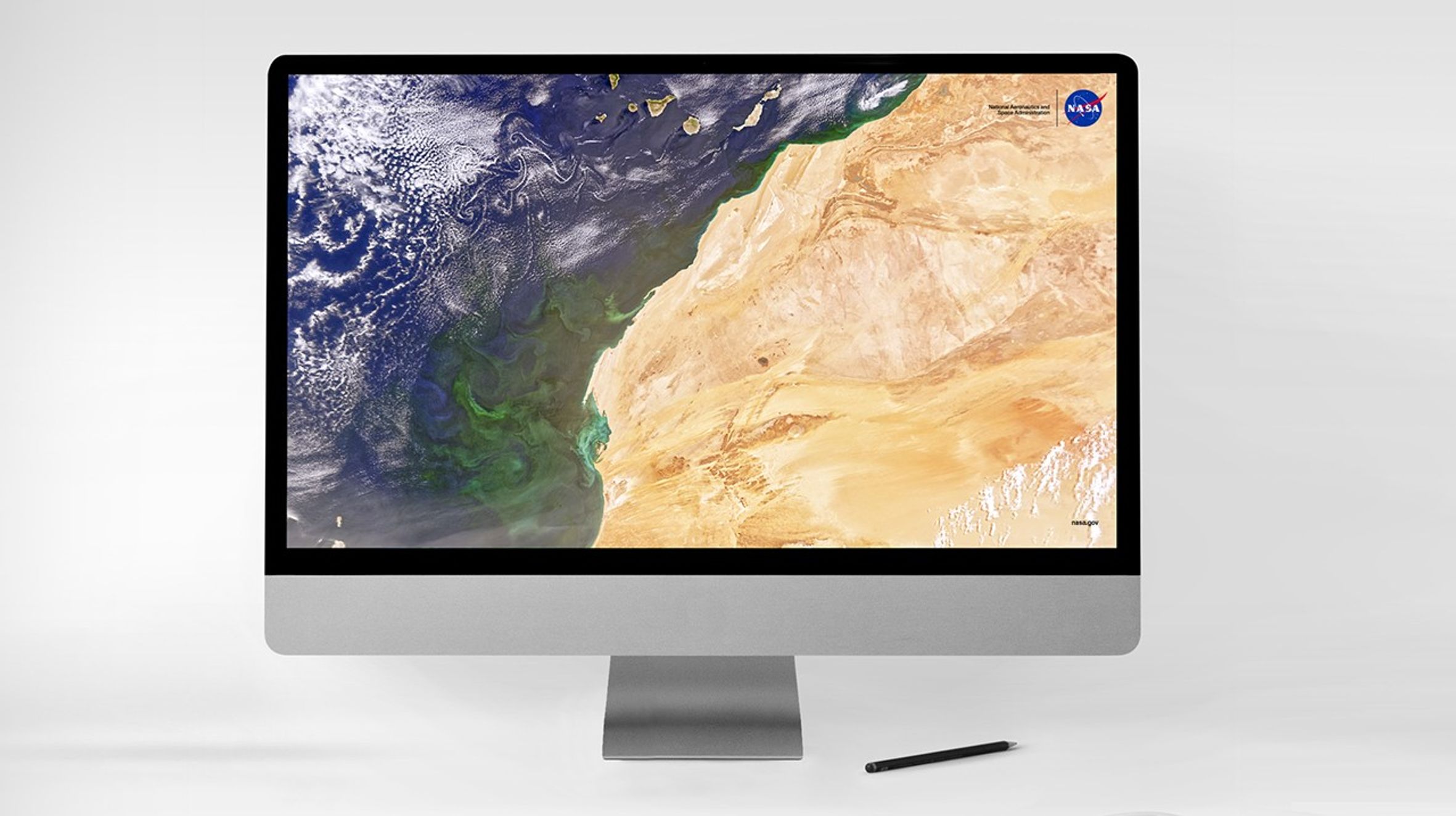 Satellite image of northwestern Africa and the Atlantic Ocean displayed on a desktop computer screen, with visible ocean currents, swirling clouds, and desert terrain; NASA logo in the corner.