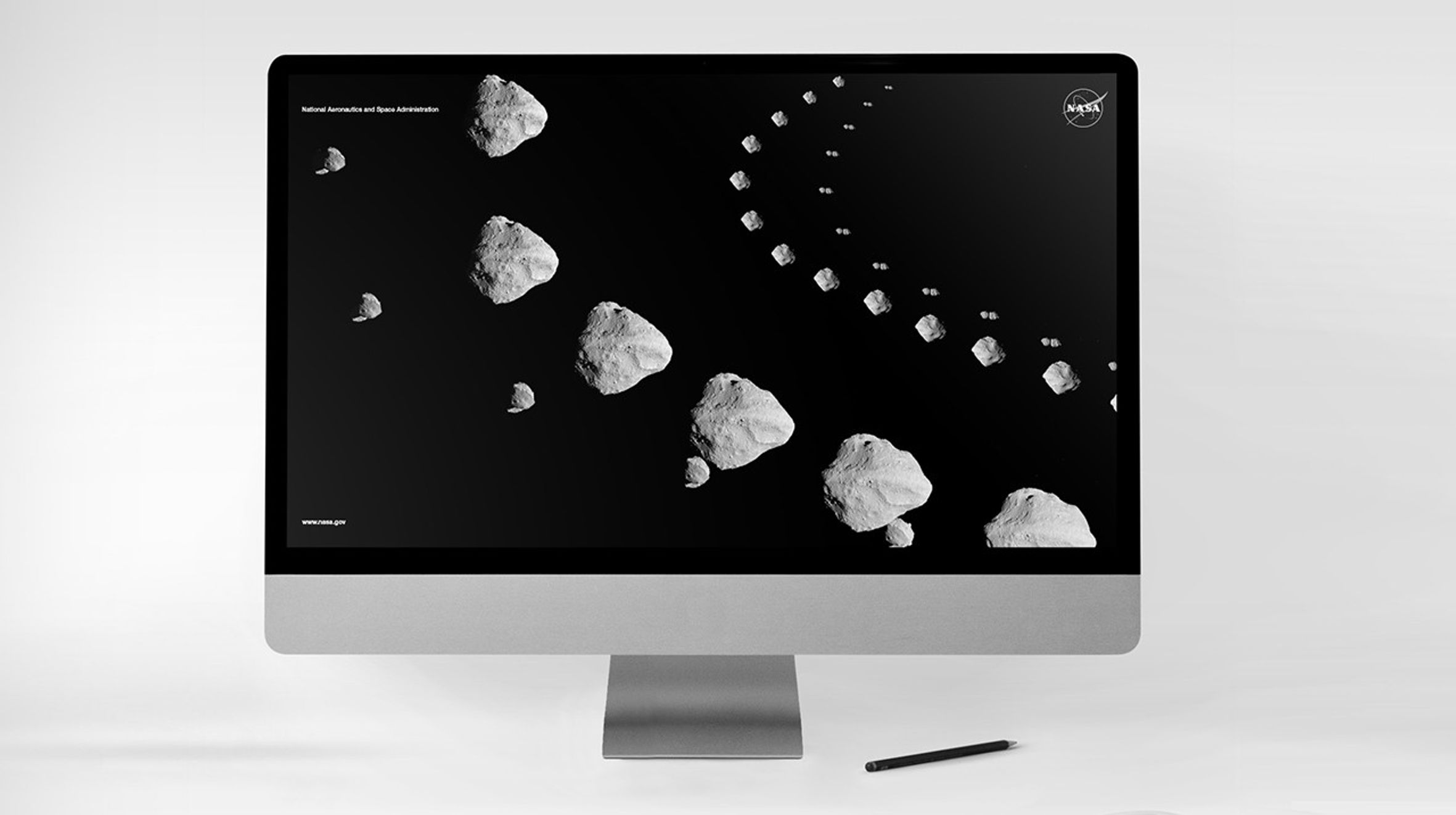A computer monitor displaying a NASA-themed digital image of asteroids arranged in a curved trajectory against a black background. The NASA logo appears in the upper right corner, and the text 'National Aeronautics and Space Administration' is visible in the upper left. The bottom left corner includes the URL 'www.nasa.gov.' A stylus pen rests on the surface below the screen.