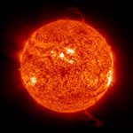 Close-up image of the Sun’s surface showing a mottled texture of glowing orange plasma, bright active regions, and several looping solar prominences extending from the edges into space.
