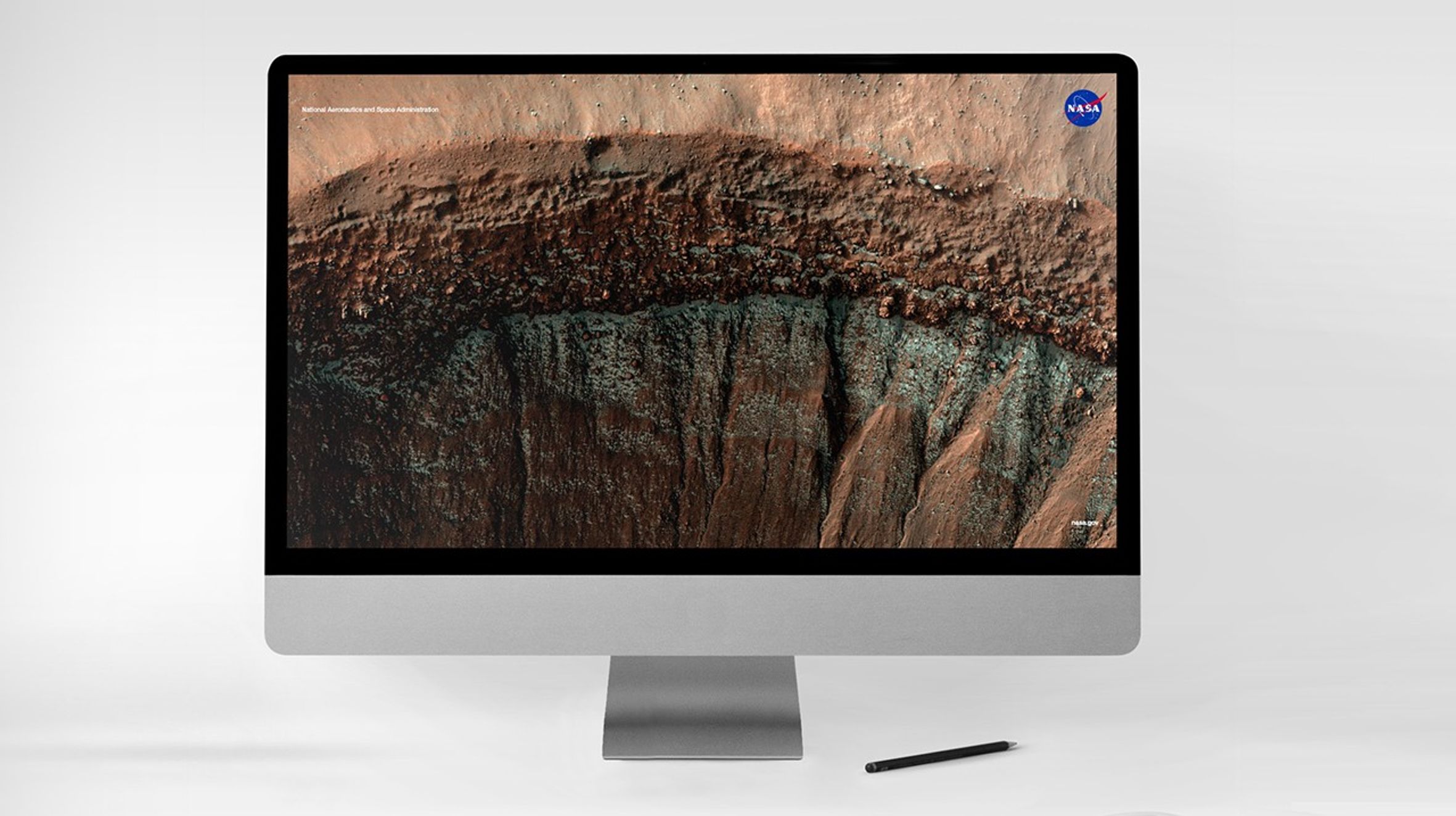 A computer monitoring displaying a high-resolution image of a Martian crater wall captured by NASA’s HiRISE camera, showing layered terrain, boulder-strewn slopes, and streaks possibly formed by past landslides or erosion.