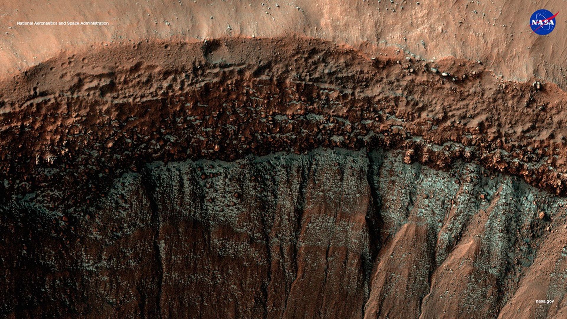 High-resolution image of a Martian crater wall captured by NASA’s HiRISE camera, showing layered terrain, boulder-strewn slopes, and streaks possibly formed by past landslides or erosion.