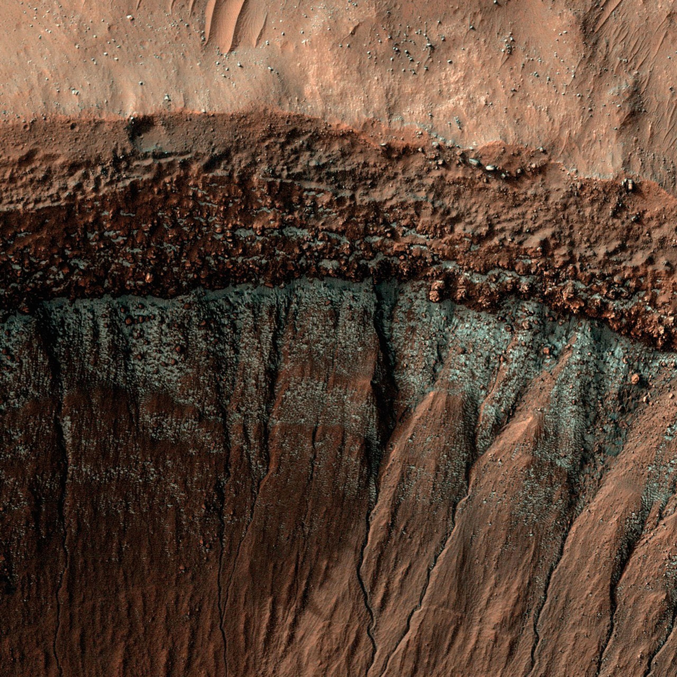 High-resolution image of a Martian crater wall captured by NASA’s HiRISE camera, showing layered terrain, boulder-strewn slopes, and streaks possibly formed by past landslides or erosion.