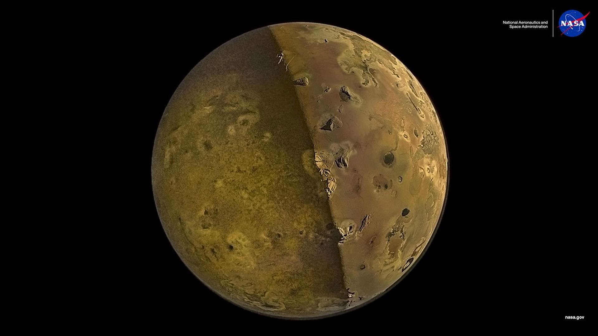 Jupiter's moon Io appearing golden-tan against the blackness of space, half the moon bathed in shadow, half in light, bisected vertically, with mountain peaks and volcanos pockmarking the surface.