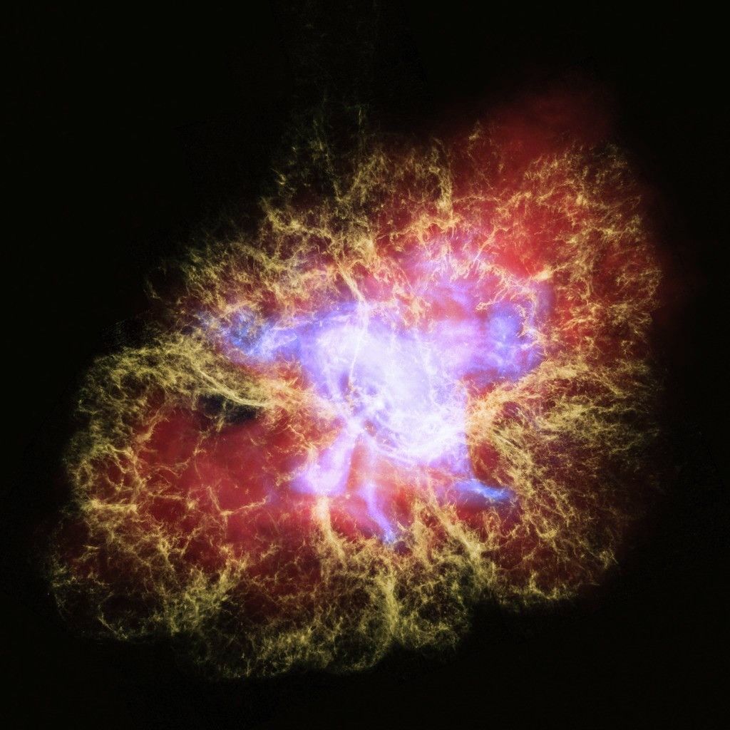 Composite image of the Crab Nebula, showing a vibrant cloud of gas and dust with filaments in yellow, red, and blue, radiating from a bright central region. The image combines data from NASA’s Hubble, Chandra, and Spitzer telescopes.