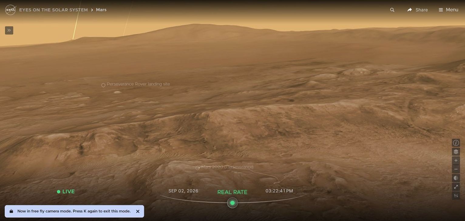 An image above the terrain of Mars far above the Perseverance rover in 3D, with text that explains the the user has entered free-fly mode by pressing "k" on their keyboard.