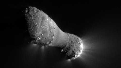 A close-up view of a peanut-shaped object with jets of material streaming out of the right end.