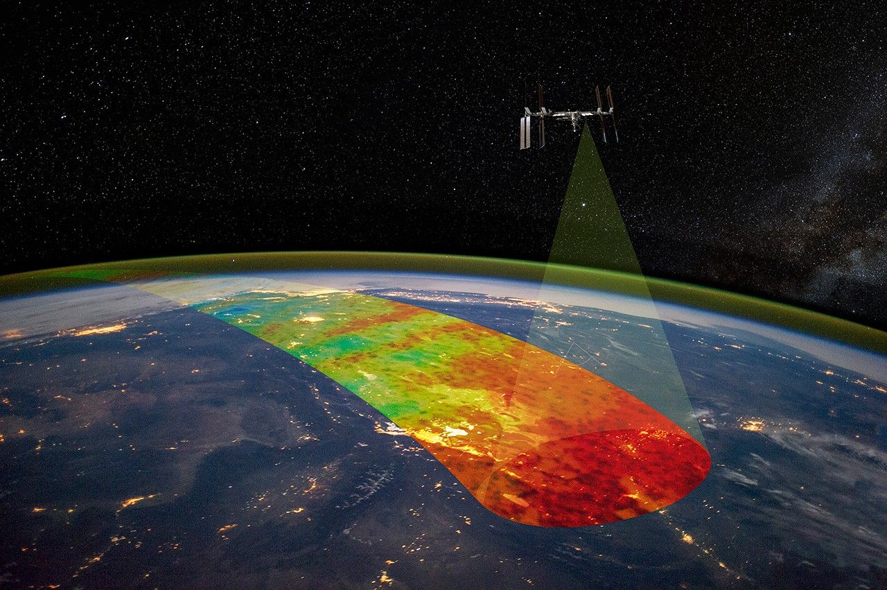 Above Earth, the International Space Station orbits. From one area toward the middle of the station, a transparent cone highlights a rainbow stripe of Earth's atmosphere.