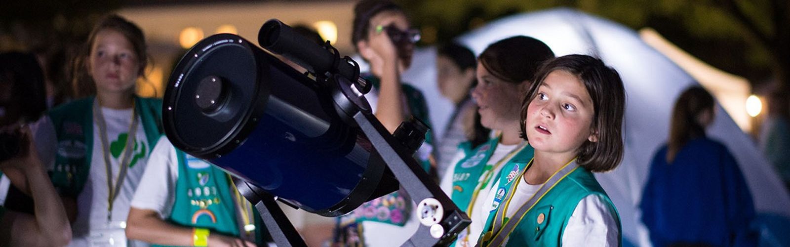 Fotografía de una "girl scout" de pie cerca de un telescopio.