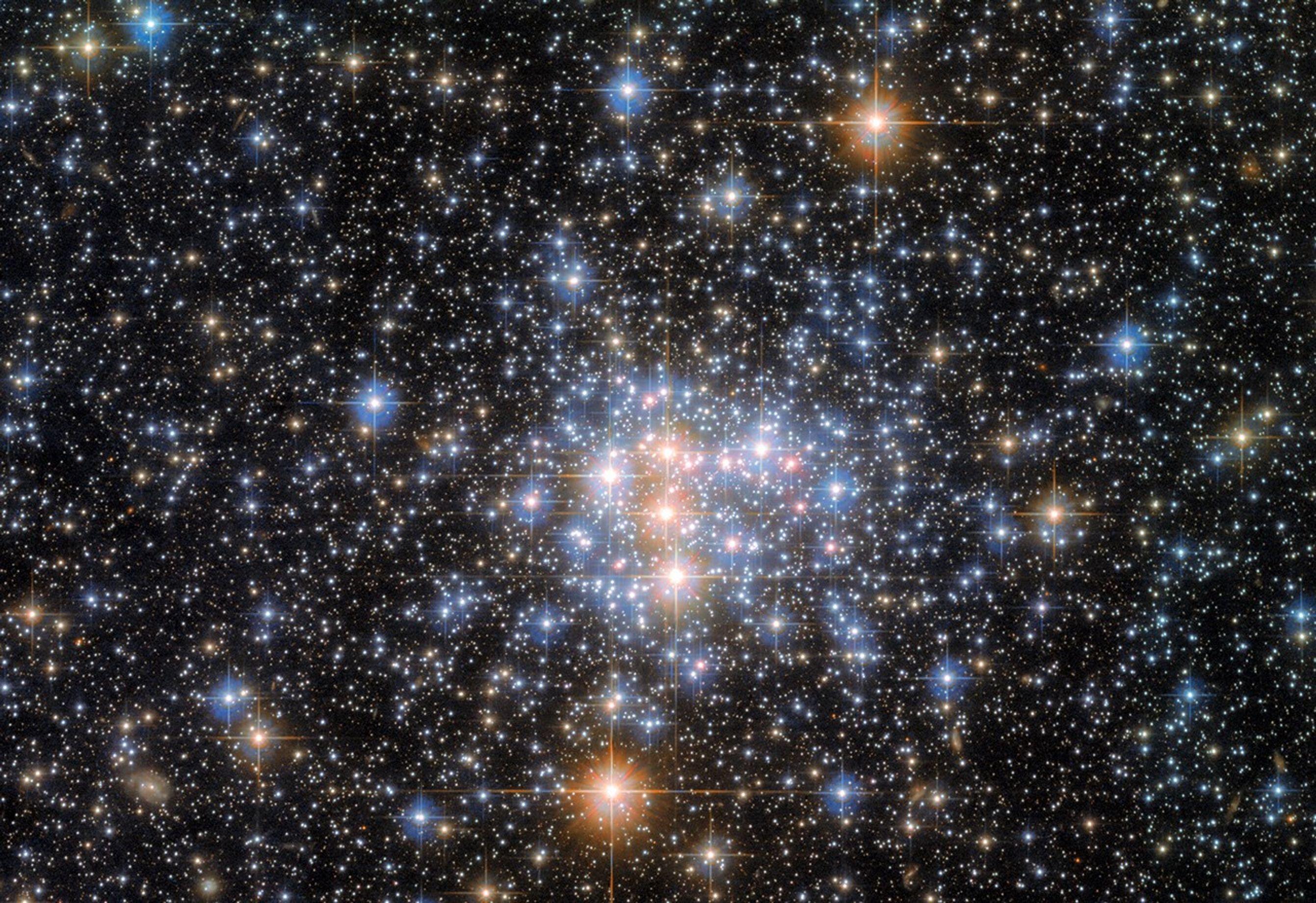Bright stars cluster at image center. they shine in shades of white, blue, and orange, and have diffraction spikes. the stars grow more sporadic at the image�s edges, and several smaller, more distant stars glow against a black backdrop of space.