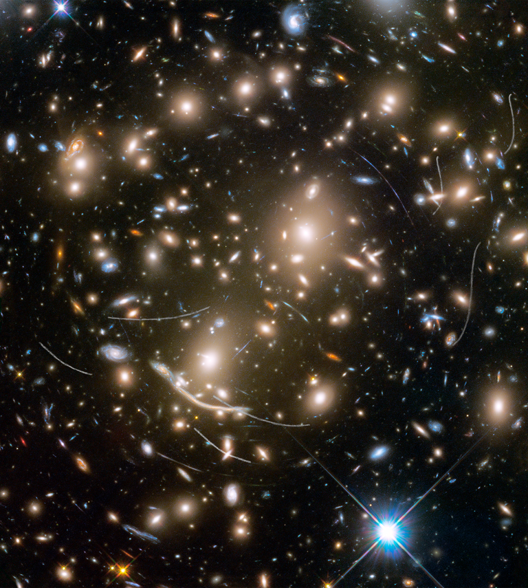 La imagen muestra un cúmulo de galaxias se ve desviando galaxias más lejanas en arcos, junto con trazas curvas en forma de S de asteroides.
