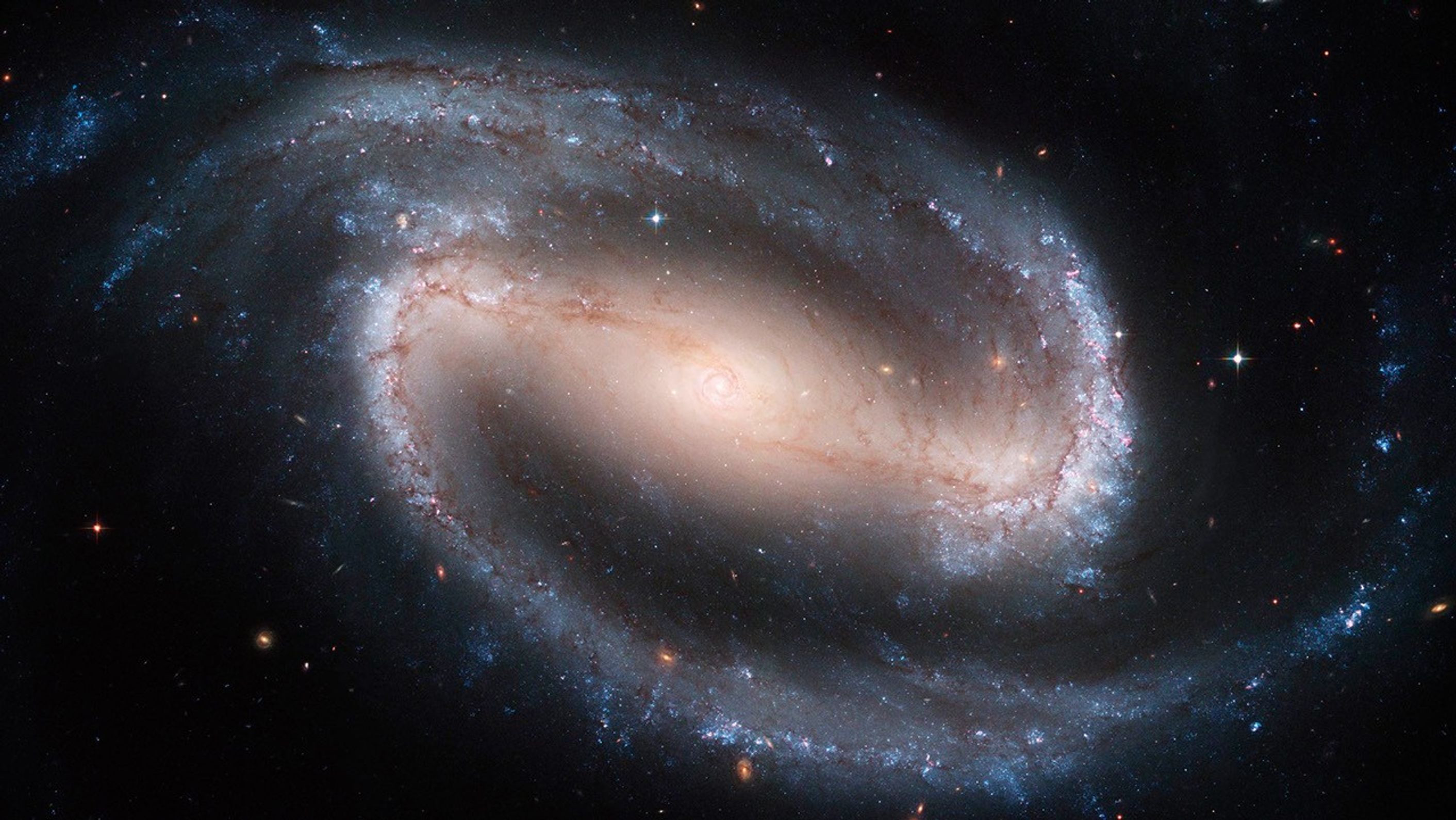 El centro de la imagen muestra un óvalo de estrellas que marcan el centro de la galaxia. Los brazos se extienden hacia la parte superior izquierda y la parte inferior derecha del bulbo central de estrellas. Más allá de los extremos de cada uno de estos brazos se extienden largas colas curvas que se arremolinan por encima y por debajo de la galaxia.