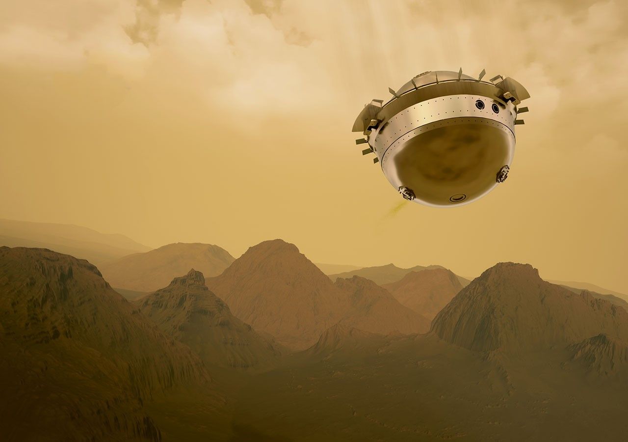 Round probe descending to Venus with hazy yellowish sky and mountains in background.