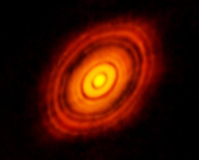 Imagen de la joven estrella HL Tau y su disco protoplanetario, obtenida por el conjunto de radiotelescopios ALMA. Esta imagen, la mejor que se haya obtenido de la formación de planetas, muestra varios anillos y espacios vacíos que anuncian la presencia de planetas emergentes a medida que estos barren el polvo y el gas en sus órbitas.