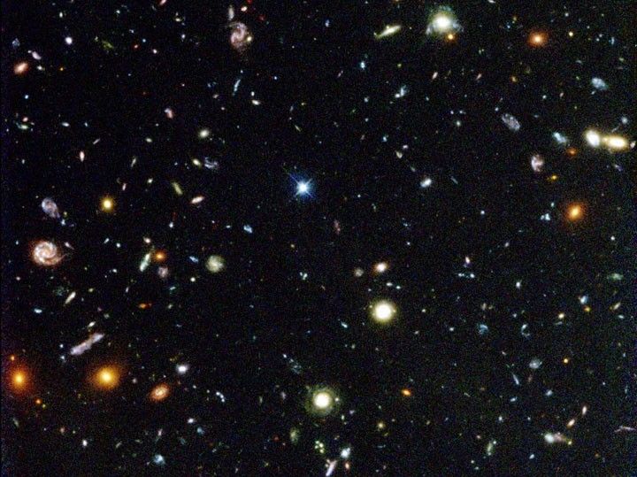 La imagen está llena de galaxias de diversas formas y tamaños. Sus colores incluyen rojo, naranja, amarillo, blanco y azul.