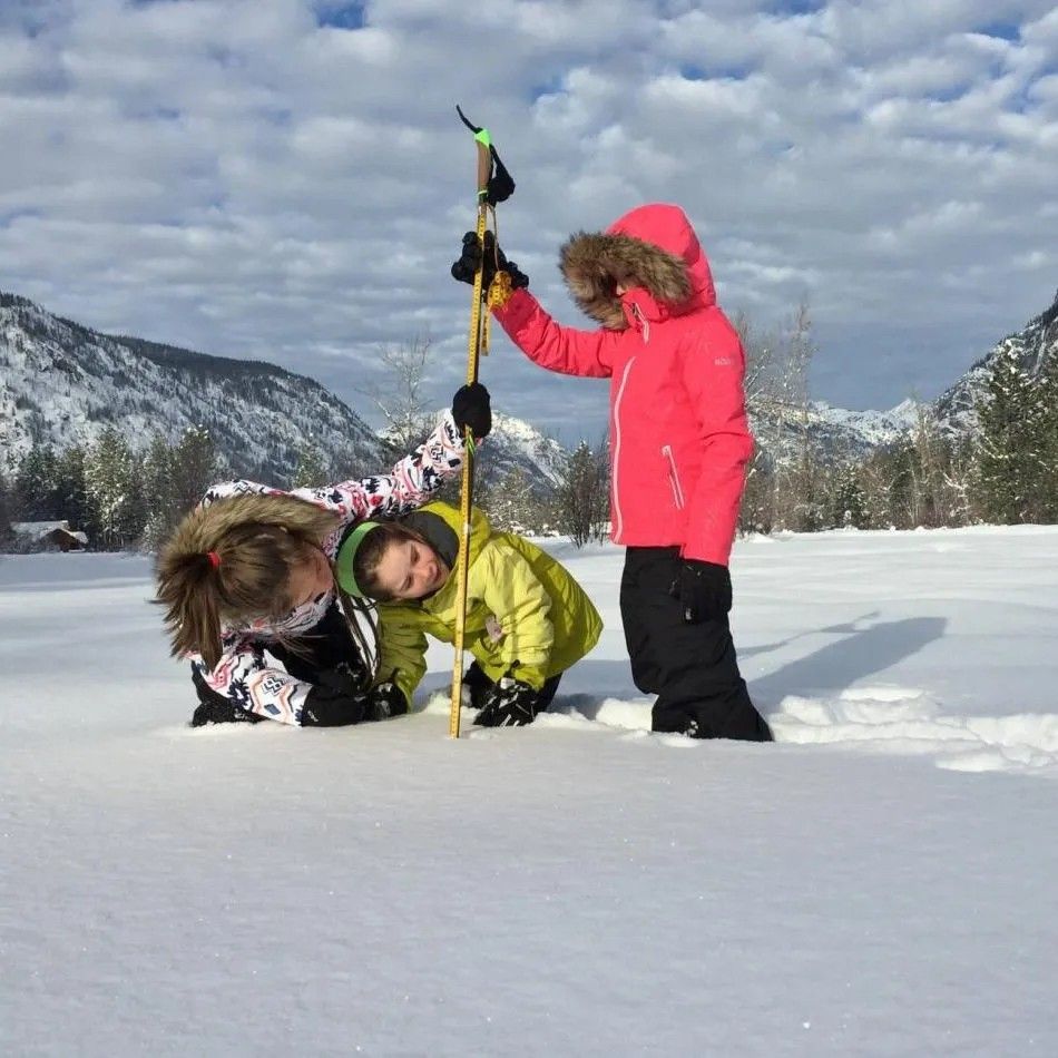 Three young girls measuring snow levels in a field of snow.