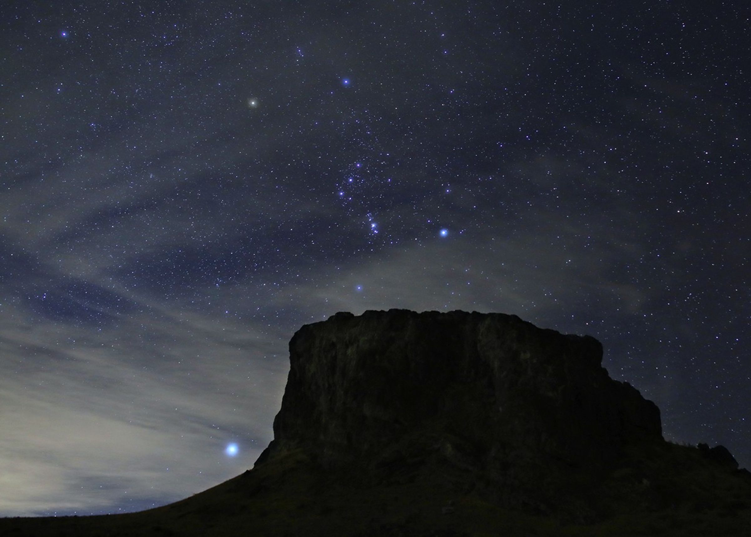 Las estrellas brillantes de la constelación de Orión aparecen por encima de una montaña por la noche. La brillante estrella Sirio se ve a la izquierda.