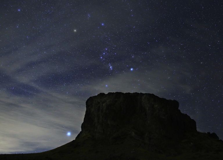 Las estrellas brillantes de la constelación de Orión aparecen por encima de una montaña por la noche. La brillante estrella Sirio se ve a la izquierda.