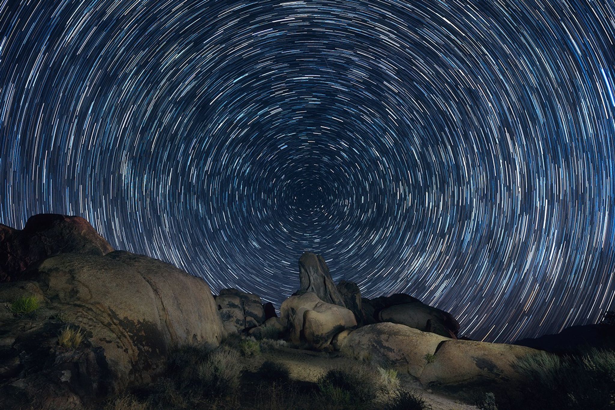 Las estelas de estrellas en el cielo giran sobre un paisaje accidentado.