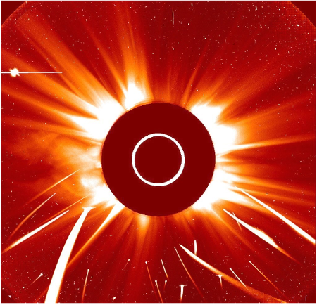 Like all SOHO data, this image is rendered in reds. A dark red occulting disk in the center of the square image blocks the bright orb of the sun. A white circle with a diameter of one third of the occulting disk indicates the size of the Sun itself. We see the sun�s corona and solar outflows emanating from behind the disk, showing bright white adjacent to the circle and cooling to dark oranges at the edge of the image. Five fat white streaks and sixteen skinny streaks, all in the bottom half of the image, represent the tracks of sungrazing comets.